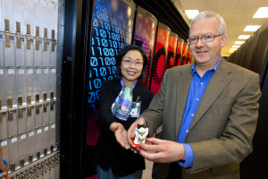 Man and woman show lucky cat figurine while standing in front of open computer system cabinet.