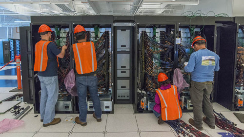 Technical workers in safety gear install the Cori Supercomputer racks and cables at NERSC.