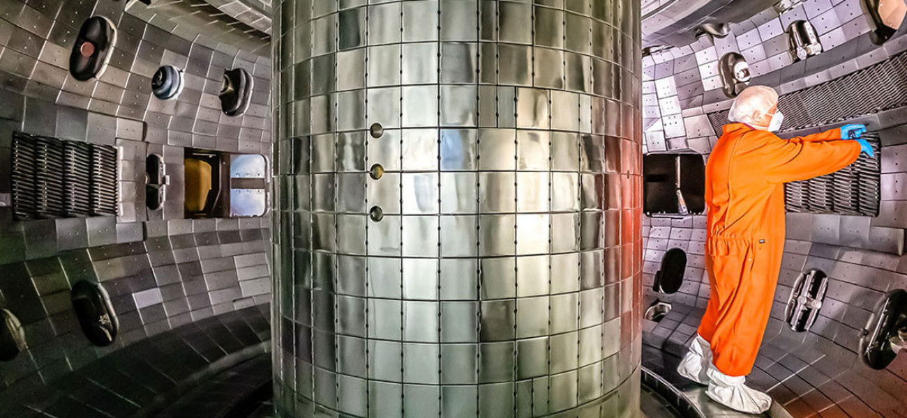 researcher in orange clean suit inside a donut-shaped, shiny metal-clad fusion reaction chamber
