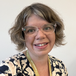 A woman with fair skin, gray hair, a glasses wearing a floral print top.