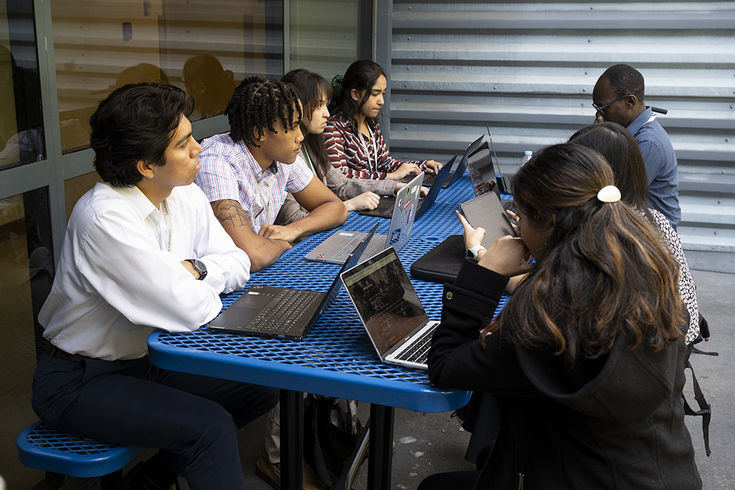 Seven men and women of different ethnicities compute on laptops as a group.