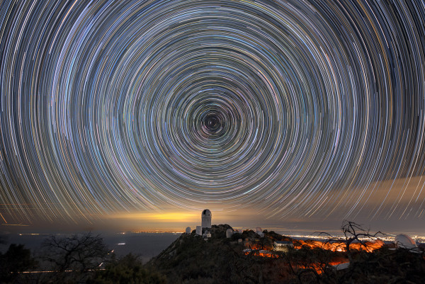 telescope on a tall peak overlooking city lights with streaks of star trails in the sky